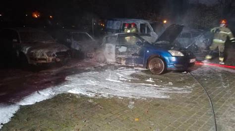 Zniszczone, spalone samochody na parkingu, otoczone przez strażaków
