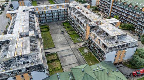 Zdjęcie spalonego poddasza lub rzędu budynków mieszkalnych po pożarze w gminie Wronki, z widocznymi strażakami w tle