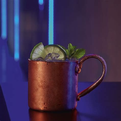 Zbliżenie na miedziany kubek Moscow Mule z kostkami lodu, plasterkiem limonki i gałązką mięty.