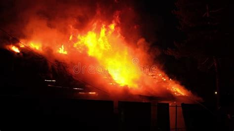 Thematic photo of a fire on a building roof at night with visible flames and smoke, firefighters' ladders reaching up