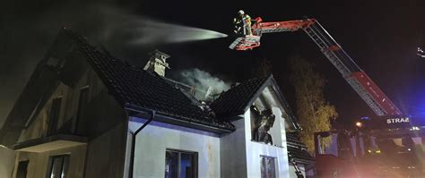 Ilustracja przedstawiająca dym unoszący się spod dachu płonącego budynku mieszkalnego w nocy