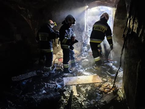 Fotografia nocnego pożaru w mieszkaniu budynku wielorodzinnego, z widocznymi ratownikami medycznymi i strażakami