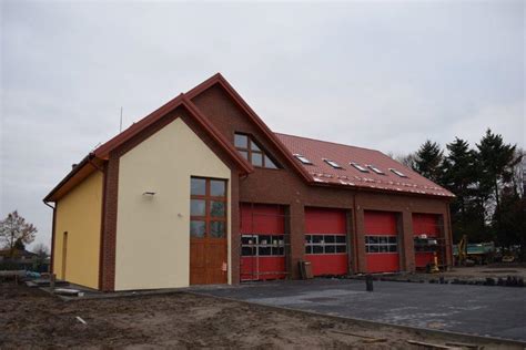 Zewnętrzny widok nowoczesnej remizy strażackiej z otwartymi bramami garażowymi i wozami strażackimi