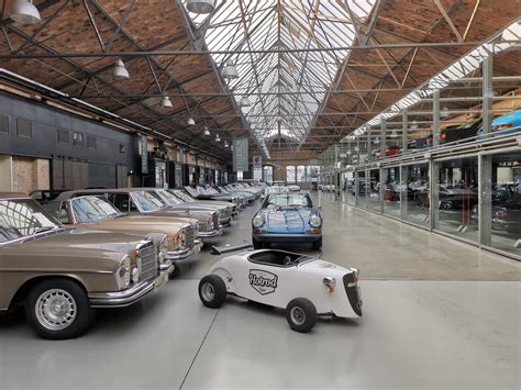 Wnętrze Classic Remise Berlin, ukazujące zabytkowe samochody w przeszklonych boksach i industrialne otoczenie