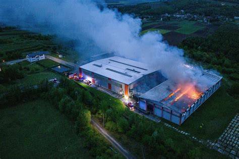 Zdjęcie strażaków gaszących pożar na sortowni odpadów, widoczne płonące hałdy śmieci i ciężki sprzęt