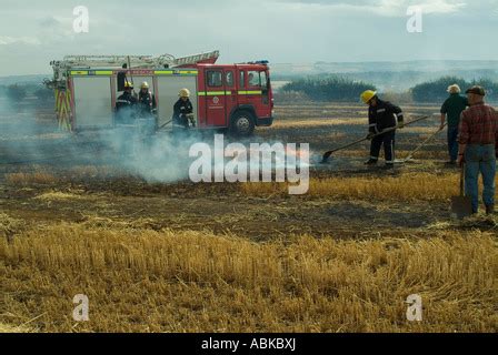 Photo of a burning baler in a field, with firefighters in the background