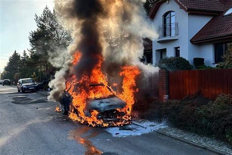 pożar samochodu BMW w nocy, płonący samochód na tle posesji