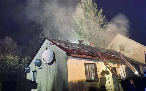 Strażacy gaszący płonący dach budynku mieszkalnego w nocy