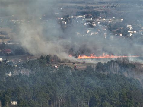 Zdjęcie dużego pożaru hali przemysłowej lub wysypiska, z gęstym dymem unoszącym się w powietrze.