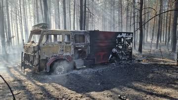 Samochód strażacki 4x4 w akcji gaszenia pożaru lasu, przejeżdżający przez trudny teren.