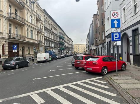 Zagrącona przestrzeń garażu podziemnego z zaparkowanymi samochodami i składowanymi obok nich rzeczami osobistymi, podkreślająca ryzyko pożarowe