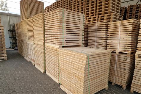 Widok na płonące składowisko drewnianych palet w nocy, z widocznymi wysokimi płomieniami i dymem