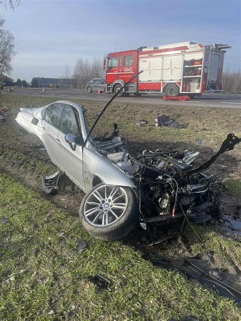 Zmasakrowane BMW po zderzeniu z drzewem, w tle służby ratunkowe