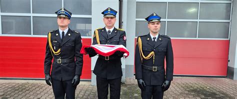 Ilustracja przedstawiająca strażaków w pełnym umundurowaniu galowym podczas uroczystości