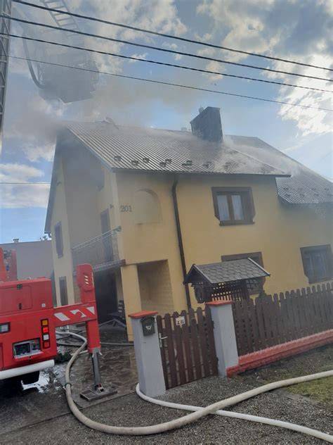 Zdjęcie przedstawiające akcję gaśniczą i dym unoszący się z poddasza płonącego domu w Gdowie