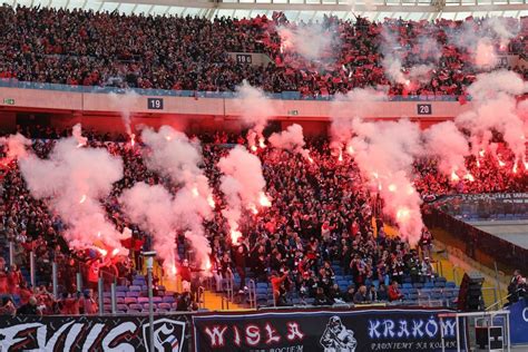 Zdjęcie kibiców Wisły Kraków z oprawą na stadionie, widoczne świece dymne lub pirotechnika
