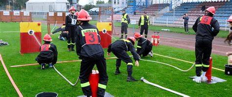 Zdjęcie zawodów sportowo-pożarniczych na stadionie, przedstawiające drużynę w trakcie wykonywania konkurencji