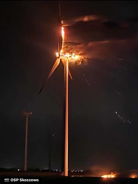 Zdjęcie przedstawiające płonącą gondolę elektrowni wiatrowej oraz spadające fragmenty łopat wirnika.