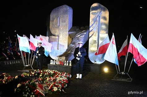 Tematyczne zdjęcie przedstawiające obchody rocznicy Grudnia 1970, znicze i wieńce pod tablicą pamiątkową