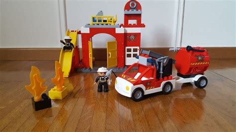 ilustracja przedstawiająca zawartość zestawu LEGO DUPLO 6168, klocki i dwie minifigurki strażaków