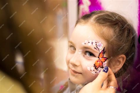 Dziecko uśmiechnięte, z częściowo pomalowaną twarzą, oglądające się w lusterku