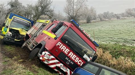 Photo of a fire truck lying on its side in a ditch, surrounded by emergency vehicles.