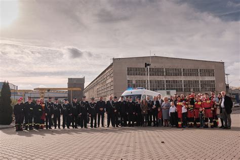 Zdjęcie przedstawiające ceremonię przekazania kluczy do nowego pojazdu strażackiego, z uczestnikami uroczystości i pojazdem w tle