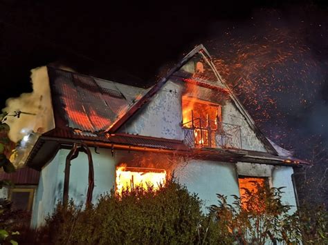 widok płonącego drewnianego domu z dachem objętym ogniem i wydobywającymi się kłębami dymu