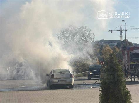 Zdjęcie płonącego samochodu osobowego na parkingu, z widocznym dymem i płomieniami