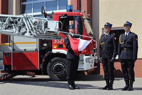 Zdjęcie strażaków w mundurach galowych blokujących drogę ozdobnym wozem strażackim podczas wesela