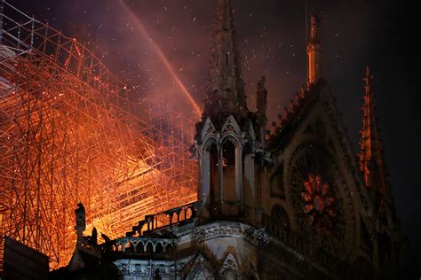 The Notre Dame Cathedral on fire at night, showing flames engulfing the roof and spire