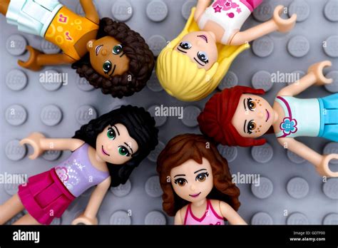 The five LEGO Friends characters (Olivia, Mia, Stephanie, Emma, Andrea) smiling, with a background showing Heartlake City. Stylized, vibrant colors.
