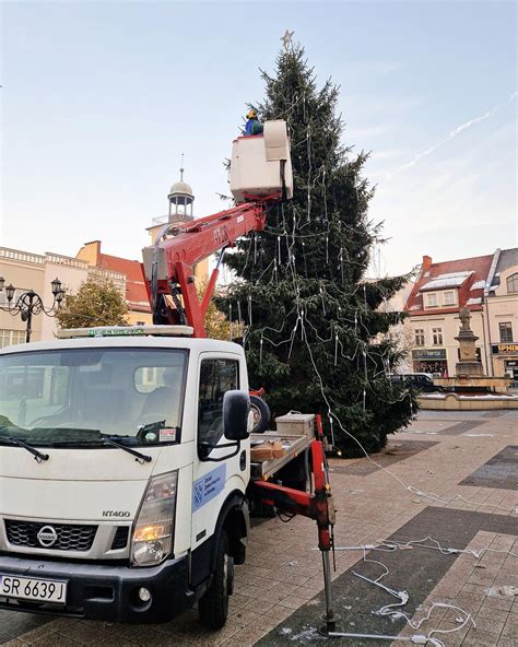 Policjanci i strażacy wspólnie z dziećmi ubierają choinkę, na której znajdują się opaski odblaskowe.