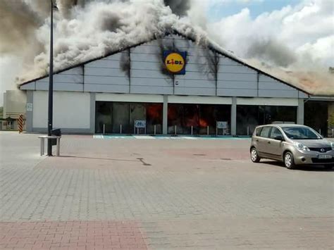 Zewnętrzny widok na palący się supermarket Lidl w Radomsku, z widocznymi płomieniami i dymem.
