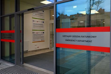 Fotografia przedstawiająca fasadę Centralnego Szpitala Klinicznego z widocznymi wozami strażackimi i strażakami na dachu lub w pobliżu budynku.