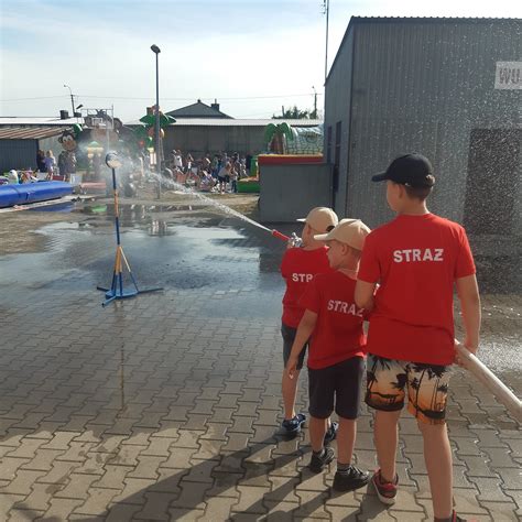 piknik strażacki z grillem i ludźmi jedzącymi kiełbaski, w tle wóz strażacki