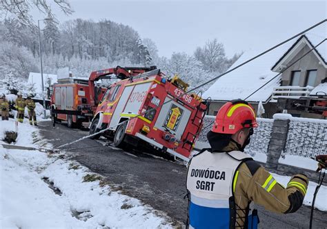 Wóz strażacki częściowo w rowie na tle drogi z plamą ropopochodną i tirem