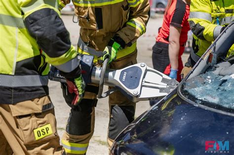 Zdjęcie młodych strażaków ćwiczących obsługę narzędzi hydraulicznych przy samochodzie