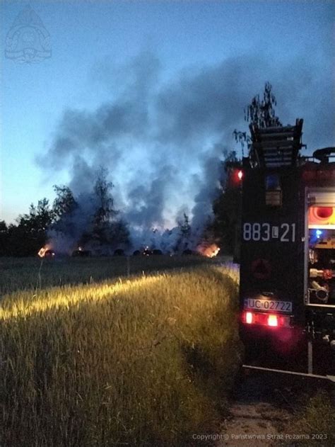 Strażacy gaszący pożar bel słomy w nocy, z widocznym sprzętem