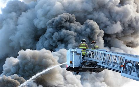 Thematic photo of a large fire emitting dense smoke, with firefighters in the foreground