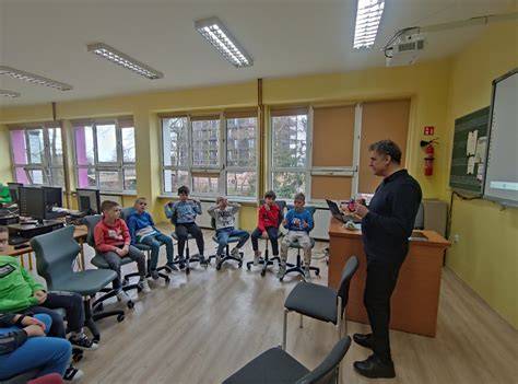 Scena z klasy, uczniowie siedzą przy biurkach. Pytanie o to, co należy zrobić po usłyszeniu alarmu w szkole, z opcjami odpowiedzi.
