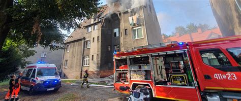 Zdjęcie przedstawiające akcję gaśniczą straży pożarnej przy kamienicy, widoczny dym i wozy strażackie