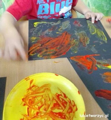 Dzieci malują palcami ogień na czarnym papierze w kolorach żółtym, czerwonym i pomarańczowym.