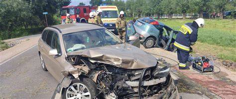 Zdjęcie miejsca kolizji dwóch samochodów osobowych, widoczne uszkodzenia pojazdów i strażacy przy pracy