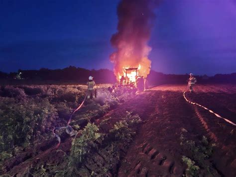 Strażacy gaszący płonący ciągnik rolniczy na polu