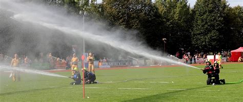 Strażacy ochotnicy podczas ćwiczeń bojowych na stadionie sportowym, w pełnym rynsztunku, operujący prądami wody