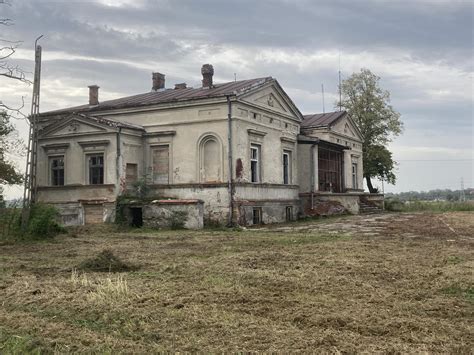 Zdjęcie pokazujące kontrast między odrestaurowanym dworkiem a piaszczystą drogą dojazdową