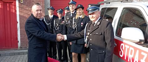 Portret prezesa OSP w mundurze galowym na tle remizy lub wozu strażackiego, symbolizujący lidera lokalnej społeczności