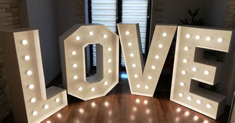 Zdjęcie przedstawiające różnorodne dekoracje i atrakcje weselne, takie jak podświetlany napis LOVE i fotobudka