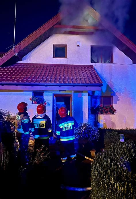 Zdjęcie przedstawiające akcję gaśniczą straży pożarnej przy płonącym domu jednorodzinnym nocą